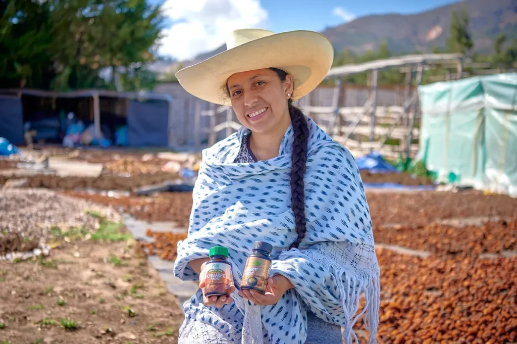 A smiling woman farmer from cajamarca standing in a green field, holding a handful of freshly harvested red Huanarpo Macho, showcasing our sustainable sourcing