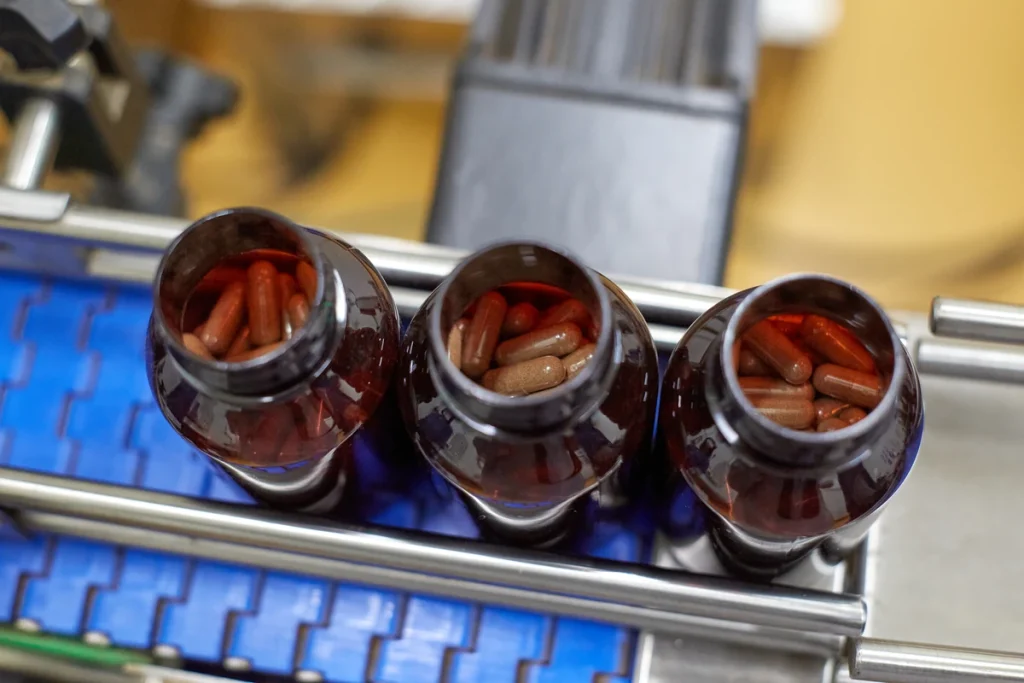 Open amber bottles filled with organic Maca capsules during manufacturing.
